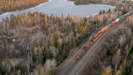 A long and colorful freight train pulling a large number of shipping and cargo containers through the Canadian shield.  Boreal forest.  Drone. 4k.