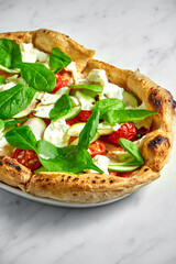 Delicious pizza with zucchini, burrata, sun-dried tomatoes, and spinach on a white plate on a white marble background