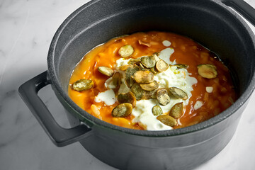 Pumpkin porridge with pumpkin seeds in green pot on light marble background