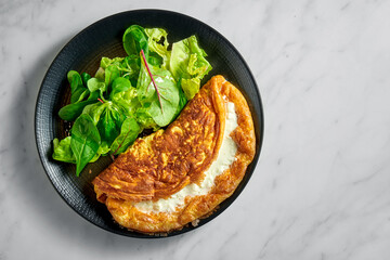 Stuffed lush creamy omelette with salad mix in black plate on white marble background