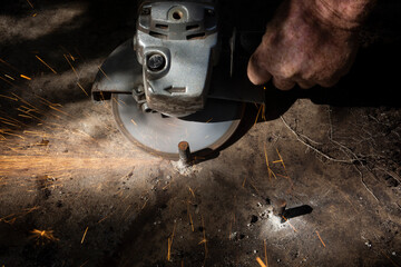A man with no protective gloves cutting a piece of steel with an angle grinder tool and a shower of bright sparks of metal spraying out.