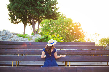 Beautiful girl in a hat sits on a bench and meets the dawn