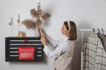 Woman millennial fashion stylist decorates a shelf with a red bag with a pampas grass vase