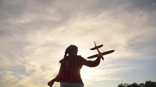 Silhouette of a happy child running in the field, holding a toy plane in his hand. Aviator girl plays at sunset in the field with a toy plane. Silhouette of a happy child aviator.