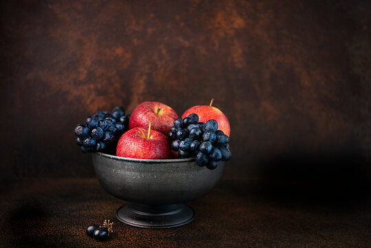 Apple and black grapes in an old bowl and dark surface 