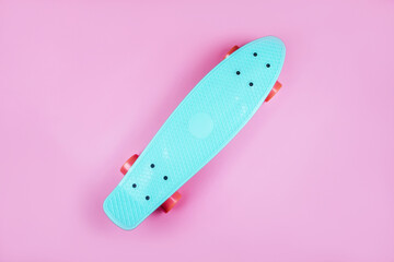 Sport inspired flatlay with turquoise penny skateboard isolated on pink background.