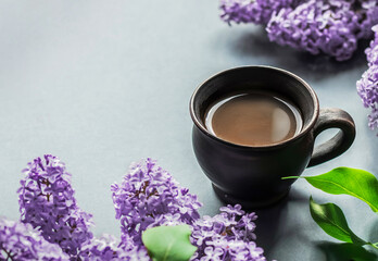 A cup of hot morning coffee and a branch of lilacs on a lilac background. Close-up concept of holidays and good morning wishes.