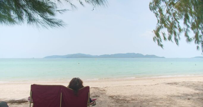 young Asian tourist woman sitting on beach chair relaxing enjoy vacation holiday weekend at beautiful tropical sor beach in sunny day summer time at Sattahip, Thailand	

