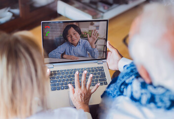 two caucasian grandparents communicate with their asian grandson through the computer. the child is...