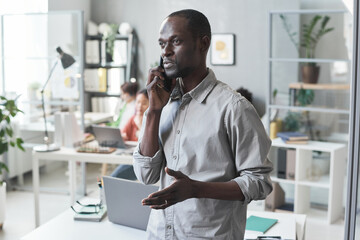 African businessman standing at office and talking with his colleague on mobile phone