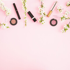 Spring white flowers with cosmetic - lipstick, shadows and mascara on pink background. Flat lay