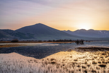 Beautiful bright sunrise over the lake and mountains, reflection in the water. Panoramic view.