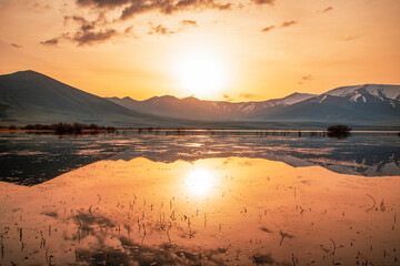 Beautiful bright sunrise over the lake and mountains, reflection in the water. Panoramic view.