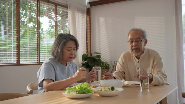Asian senior couple feeling lonely while eating food on dining table.