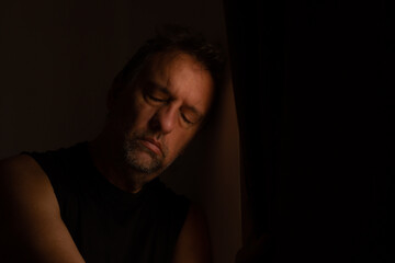 Caucasian middle-aged man in a dark room with depression. Concept of confinement in times of pandemic. Psychiatric or psychological illness.