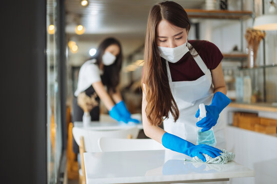 Waitress wearing face mask cleaning table disinfectant spray in in coffee shop restaurant