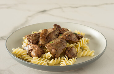 Italian whole grain pasta with roasted chicken liver and onions served on a plate on marble background