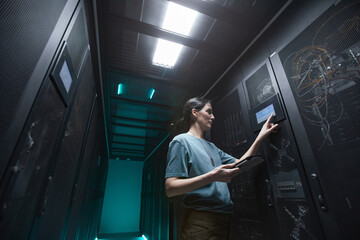 Low angle portrait of military woman using control panel while setting up servers in data center,...