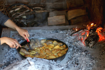 Unrecognizable person preparing meat and potatoes under the iron bell ('peka') in the fireplace....