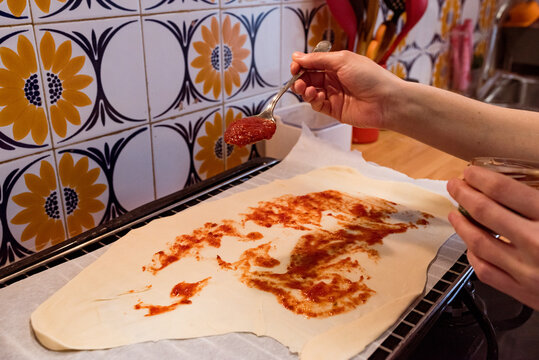 Hand about to pour a tablespoon of fried tomato on the base of a dough to prepare a pizza