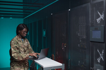 Waist up portrait of young African-American woman wearing military uniform using computer while...