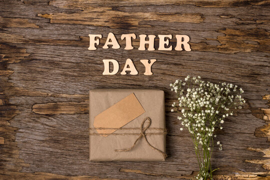 Gift box in brown paper with the inscription with wooden letters Father's Day on a wooden background. Flat lay. Father's day gift for dad. Father's Day holiday concept in 2021.
