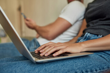 Young woman's hands on laptop in front, man's hands with smartphone on background