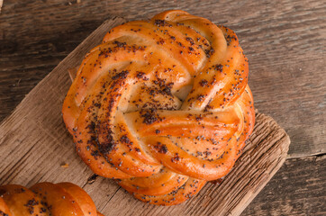 Fresh baked goods - delicious wicker bun with poppy seeds close-up on a wooden