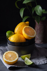 juicy lemons and limes in a black bowl on a gray table. Dark and mood concept