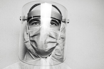 Black and white studio portrait of doctor man wearing PPE suit against coronavirus and covid-19, on the background of grey wall. Pandemic concept.