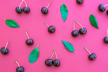 Cherries and green leaves pattern on deep pink background. Pattern of cherry with green leaves. Abstract food background. Top view, flat lay.