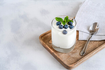White yogurt in glass with fresh blueberry on a wooden tray. Homemade Greek yogurt in a glass