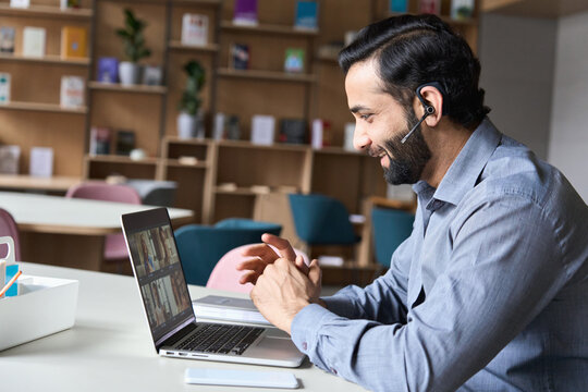 Latin indian smiling businessman wearing headset having virtual team meeting group call chatting with diverse people in customer support. Video conference call on computer with manager and employees.