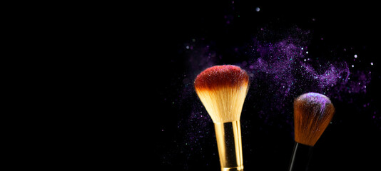 Cosmetics brushes and explosion purple makeup powder. Makeup brush with colorful powder mixed in explosion on black background close up. Beauty product eye shadows or blusher concept. Copy space