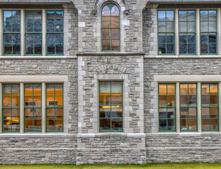 Exterior view of facade of old limestone building looking through lit paned windows, nobody