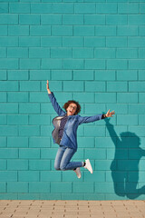 Front view of a happy woman jumping against a bright blue wall on a sunny day