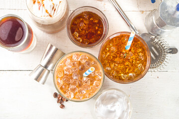 Set with different iced summer coffee drinks - espresso, frappe, latte, cappuccino, with whipped cream, syrup and crushed ice, in various glasses and mugs on white background copy space