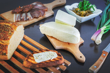 Haloumi cheese with freshly grilled bread with green onions, smoked ham, sausage, olives on a dark wooden dining table.