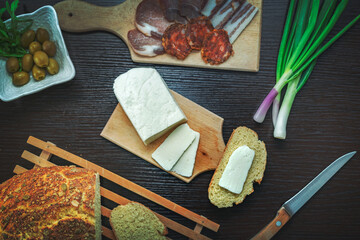 Haloumi cheese with freshly baked bread with green onions, smoked ham, sausage, olives on a dark wooden dining table.Top view