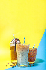 Set with different iced summer coffee drinks - espresso, frappe, latte, cappuccino, with whipped cream, syrup and crushed ice, in various glasses and mugs on trendy bright yellow blue background