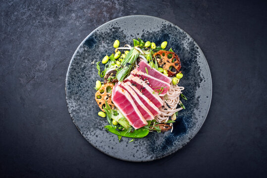 Modern style traditional Japanese gourmet seared tuna fish steak tataki with soba noodles and stir-fried vegetables served as top view on a Nordic design plate with copy space