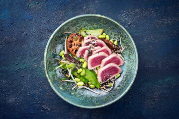 Modern style traditional Japanese gourmet seared tuna fish steak tataki with soba noodles and stir-fried vegetables served as top view on a Nordic design plate with copy space