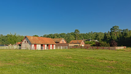 Fototapeta na wymiar Horse stables in traditional brick stone style and meadows on a sunny day in Oise region, France, high angle view 