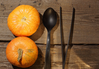 Two pumpkins lie on a wooden table next to black cutlery