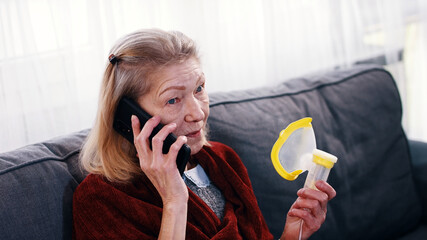 Elderly woman using oxygen inhaler while speaking on the phone. Coronavirus outbreak and vulnerable group of people. High quality photo - obrazy, fototapety, plakaty