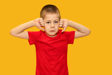 Child in red t-shirt on yellow background, boy 5 years old, sad. Shows fingers down. Sad children's emotions