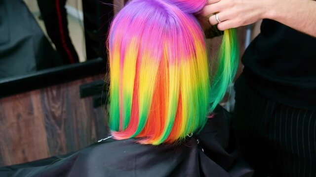 The hairdresser dyes the hair of a blonde woman in different bright colors