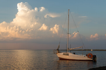 Small white yacht docked by the coast against an evening sky with big cloud. Sunset over Black sea, summer time. Family vacation or travel by sea on own yacht.