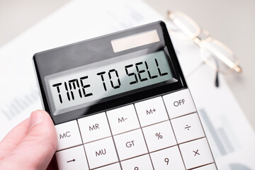 The word TIME TO SELL is written on the calculator. Business man holding a calculator in his hand.