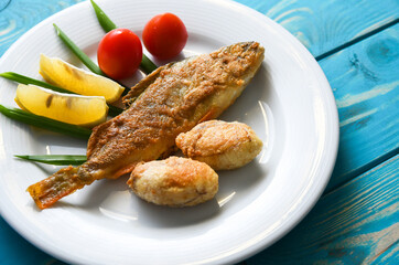 Fried fish on a plate with vegetables, lemon and onion